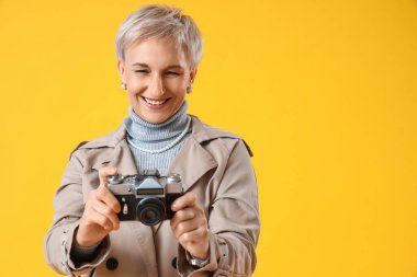 Sarı arka planda fotoğraf makinesi olan güzel olgun bir kadın.