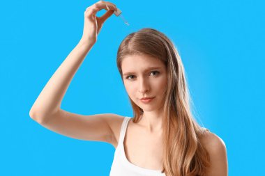 Mavi arka planda saç uzatmak için serum kullanan genç bir kadın.