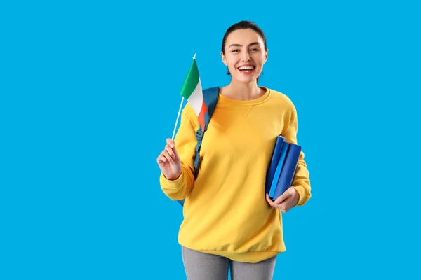 Young woman with flag of Ireland and books on blue background