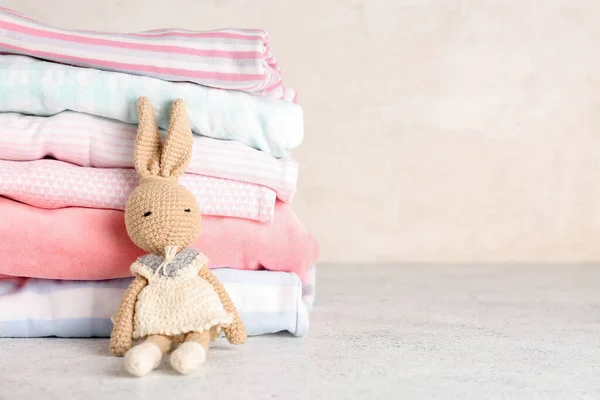 Stack of baby clothes with knitted toy on light background