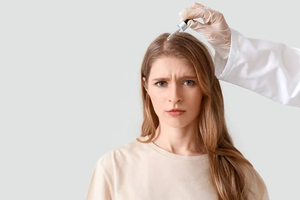 美容师用血清治疗年轻女子浅色背景的头发 — 图库照片
