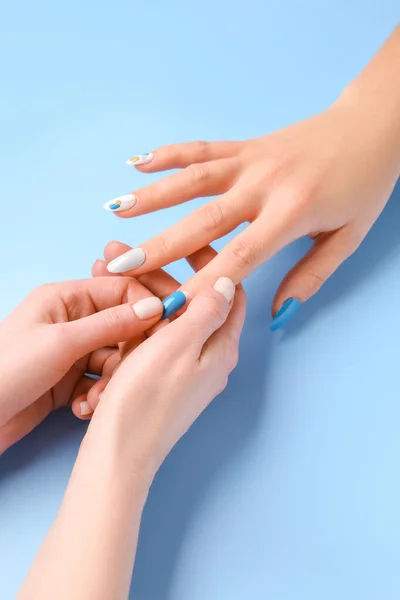 Manicure master applying press-on nail on blue background, closeup