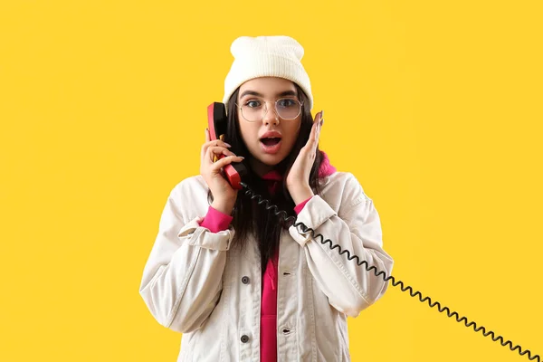 Surprised young woman with telephone receiver on yellow background