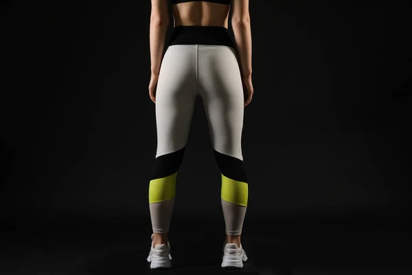 Sporty young woman in leggings on black background, back view