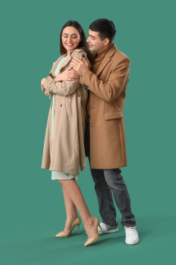 Genç adam yeşil arka planda kız arkadaşına sarılıyor.