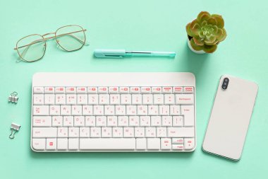 Turkuaz arka planda gözlük, klavye, cep telefonu ve ev bitkisi bileşimi