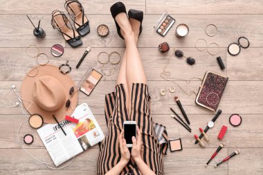 Hafif ahşap zeminde cep telefonu kullanan aksesuarları ve makyaj malzemeleri olan bir kadın.