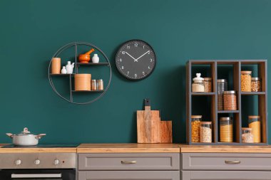 Mutfak tezgahında farklı yiyeceklerle birlikte yeşil duvarın yanında tencere, tahta ve raf kesme ünitesi.