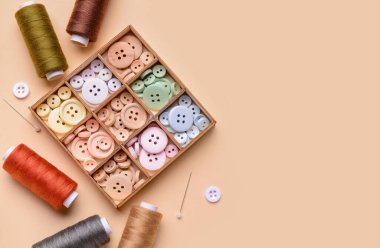 Renk arkaplanı üzerinde farklı düğmeler, iplik makaraları ve top lobutları olan kompozisyon