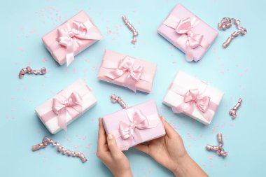 Mavi arka planda kadın eli, hediye kutusu, yılan yağı ve konfeti olan kompozisyon