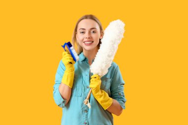 Young woman with cleaning brush and pp-duster on yellow background clipart