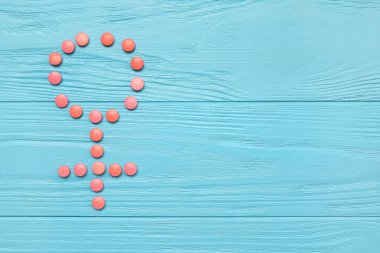 Mavi ahşap arka planda hormonal haplarla yapılan kadın sembolü.