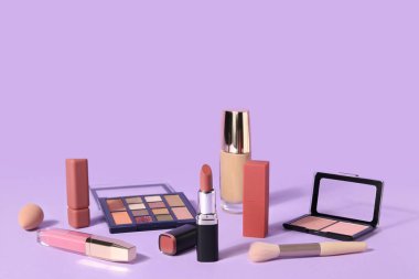 Leylak arka planında farklı kozmetik ürünleri ve ruj.