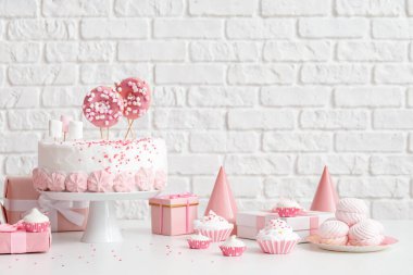 Tuğla duvarın yanındaki beyaz masada şekerli doğum günü pastası