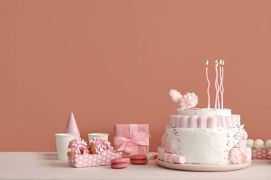 Koyu bej duvarın yanındaki beyaz masada mumlar ve şekerler olan doğum günü pastası.
