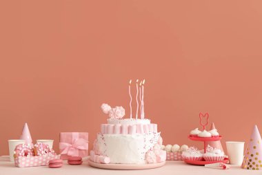 Koyu bej duvarın yanındaki beyaz masada mumlar ve şekerler olan doğum günü pastası.