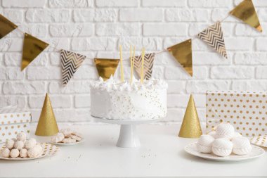 Doğum günü pastası, tuğla duvarın yanındaki beyaz masada mumlar ve şekerler.