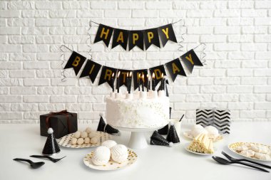 Doğum günü pastası, beyaz masada mumlar ve tuğla duvarda çelenkler.