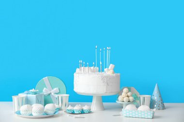 Mavi duvarın yanındaki beyaz masada mumlu ve şekerli doğum günü pastası.