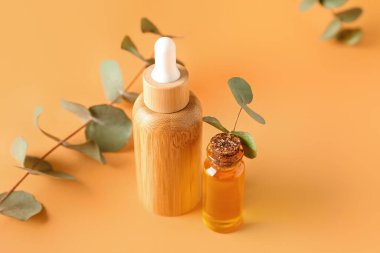 Sarı arka planda okaliptüs dalları olan kozmetik yağı şişeleri.