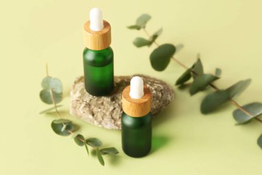 Okaliptüs dalları ve yeşil masa üzerinde taş olan kozmetik yağları.