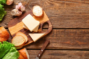 Kahverengi ahşap zemin üzerinde işlenmiş peynir, ekmek ve sarımsak olan tahta.