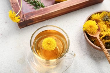 Beyaz arka planda çiçekli bir bardak sağlıklı karahindiba çayı ve kase.