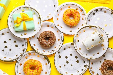 Sarı arka planda doğum günü hediyesi ve çörekli tek kullanımlık kağıt masa takımı.