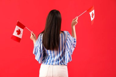 Kırmızı arka planda Kanada bayrakları olan genç bir kadın.