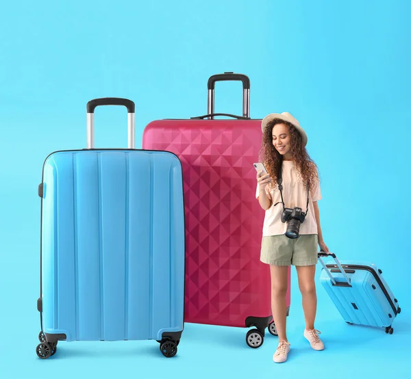 African-American female tourist with phone and big suitcases on light blue background