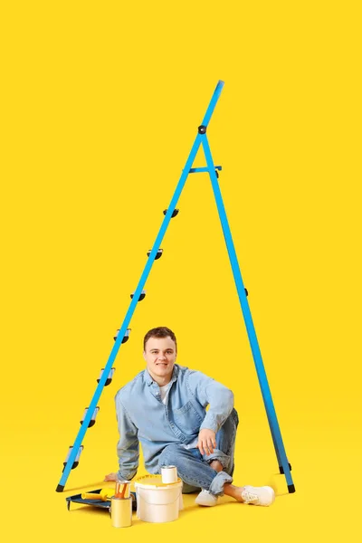 Young Man Ladder Cans Paint Sitting Yellow Background — Stock Fotó
