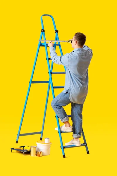 Jonge Man Meten Ladder Gele Achtergrond — Stockfoto