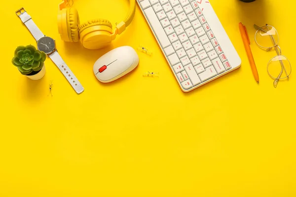 Composition with keyboard, headphones, glasses and houseplant on yellow background