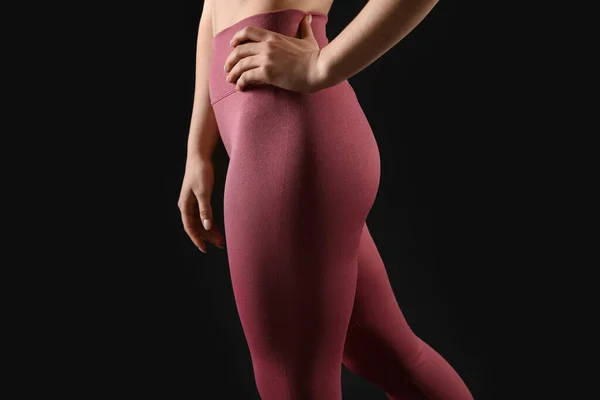 Sporty young woman in leggings on black background, closeup
