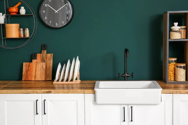 Sink and dish rack with plates on kitchen counter near green wall