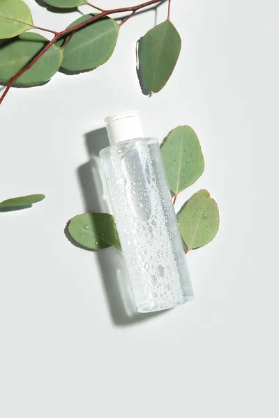 stock image Bottle of micellar water with eucalyptus branches on light background