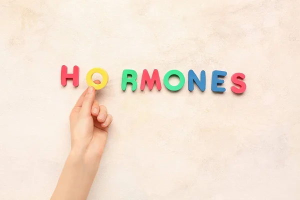 Female hand and word HORMONES on light background