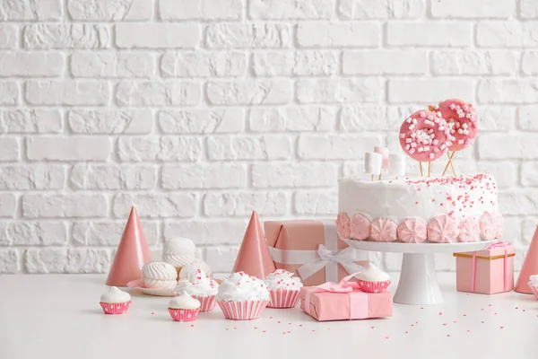レンガの壁の近くの白いテーブルの上にお菓子と誕生日ケーキ — ストック写真