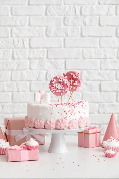 レンガの壁の近くの白いテーブルの上にお菓子と誕生日ケーキ — ストック写真