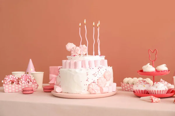 濃いベージュの壁の近くの白いテーブルの上にキャンドルやお菓子と誕生日ケーキ — ストック写真