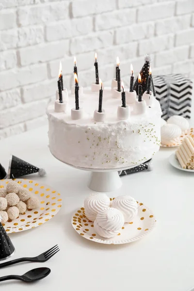 レンガの壁の近くの白いテーブルの上にキャンドルやお菓子と誕生日ケーキ — ストック写真