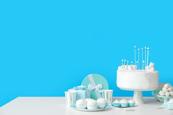 青い壁の近くの白いテーブルの上にキャンドルやお菓子と誕生日ケーキ — ストック写真