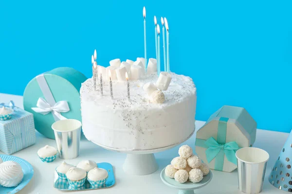 青い壁の近くの白いテーブルの上にキャンドルやお菓子と誕生日ケーキ — ストック写真