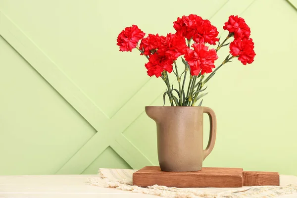 Vase with red carnations on white wooden table near light green wall