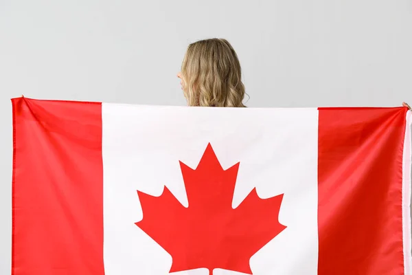 Young woman with flag of Canada on light background, back view