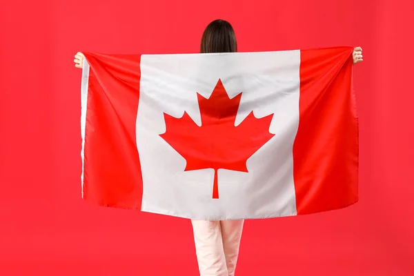 Young woman with flag of Canada on red background, back view