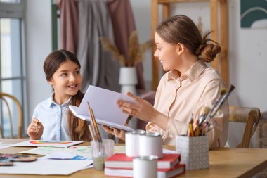 Kitabı olan bir öğretmen atölyedeki küçük kıza özel resim dersi veriyor.