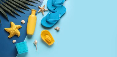 Mavi arka plandaki çocuklar için güneş kremi, plaj oyuncakları ve parmak arası terlikler.