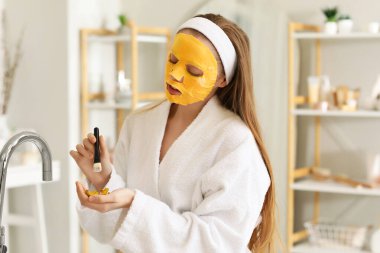 Çarşaf maskeli, zerdeçal kökleri ve banyoda fırçası olan genç bir kadın.