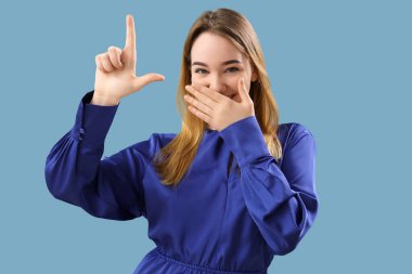 Young woman showing loser gesture on blue background clipart